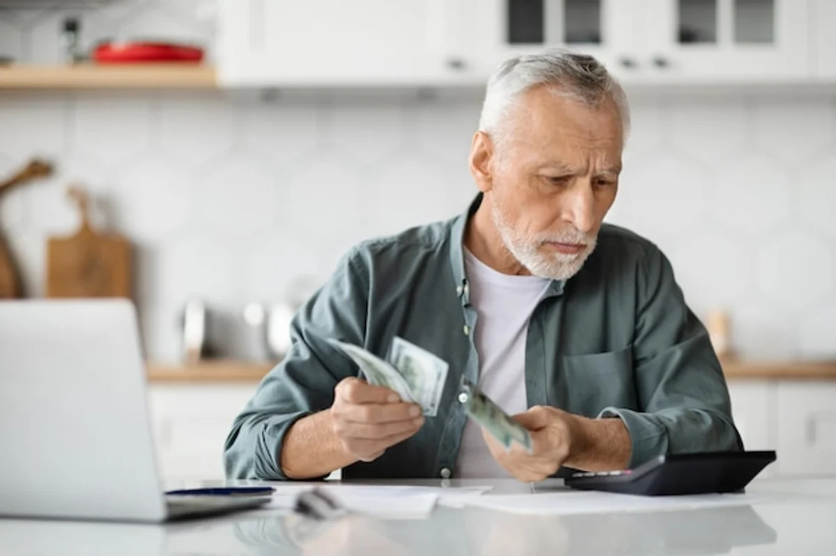 senior reviewing finances at kitchen table with documents and calculator