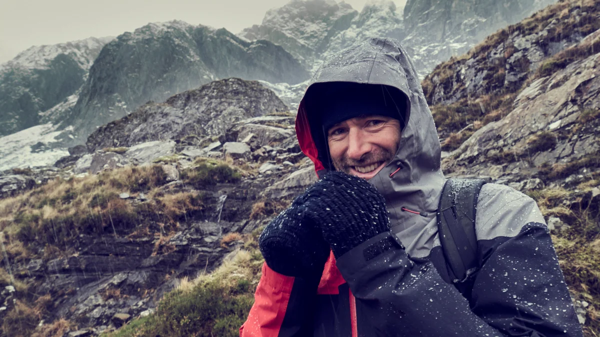 person putting on waterproof hiking jacket in rain mountain trail germany